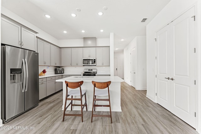 kitchen with an island with sink, light hardwood / wood-style floors, a breakfast bar area, gray cabinets, and appliances with stainless steel finishes