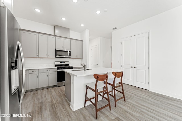 kitchen with appliances with stainless steel finishes, a kitchen breakfast bar, a kitchen island with sink, sink, and gray cabinets