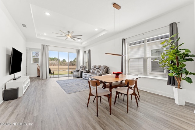 dining space featuring ceiling fan, light wood-type flooring, and a tray ceiling