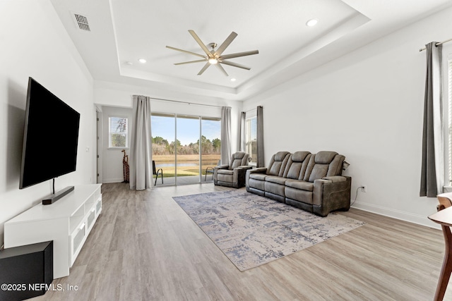 living room with light hardwood / wood-style floors, a raised ceiling, and ceiling fan