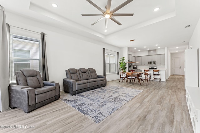 living room featuring light hardwood / wood-style floors, a raised ceiling, ceiling fan, and plenty of natural light