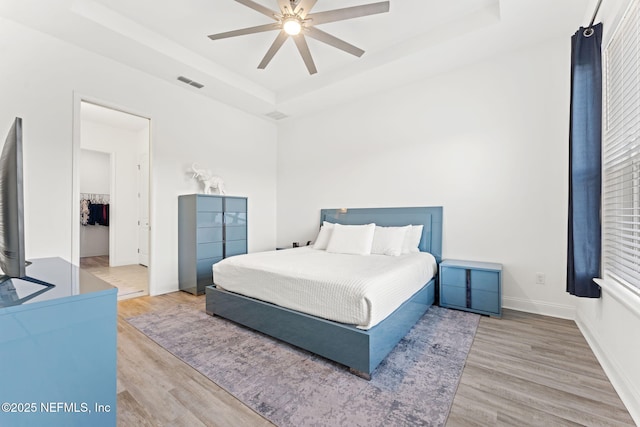 bedroom with light wood-type flooring, a tray ceiling, and ceiling fan