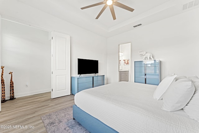 bedroom featuring hardwood / wood-style flooring, ceiling fan, connected bathroom, and a tray ceiling