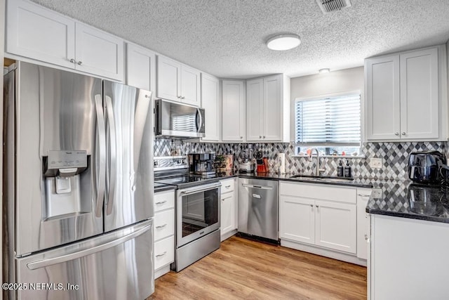 kitchen featuring dark stone counters, sink, light wood-type flooring, appliances with stainless steel finishes, and white cabinetry