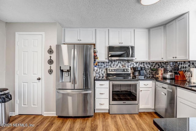 kitchen featuring light hardwood / wood-style flooring, white cabinets, dark stone counters, and appliances with stainless steel finishes