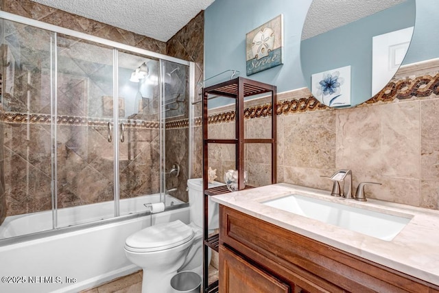 full bathroom featuring vanity, a textured ceiling, shower / bath combination with glass door, tile walls, and toilet