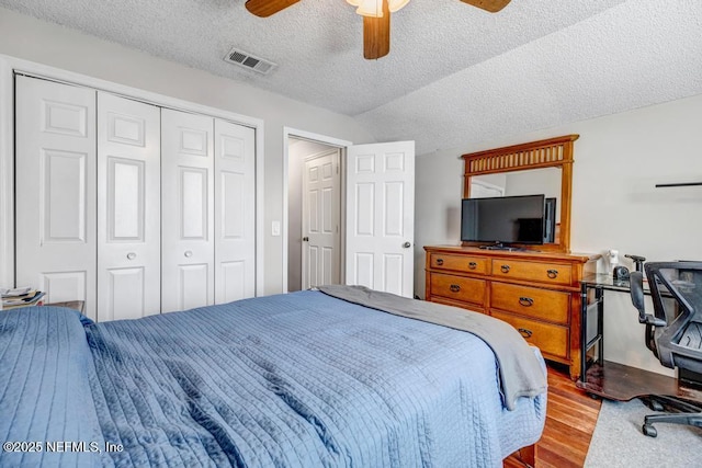 bedroom with a textured ceiling, vaulted ceiling, ceiling fan, light hardwood / wood-style floors, and a closet