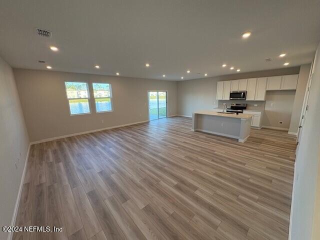 kitchen with white cabinets, light wood-type flooring, stainless steel appliances, and an island with sink