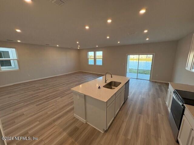 kitchen featuring sink, an island with sink, white cabinetry, and electric stove