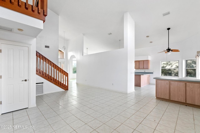 unfurnished living room with ceiling fan, light tile patterned flooring, and a towering ceiling