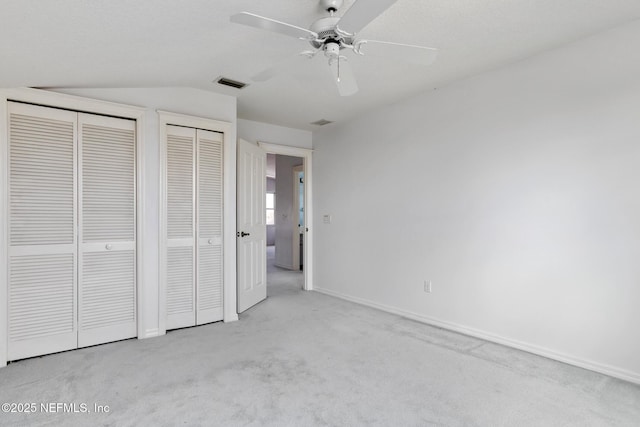 unfurnished bedroom with ceiling fan, vaulted ceiling, light carpet, and multiple closets