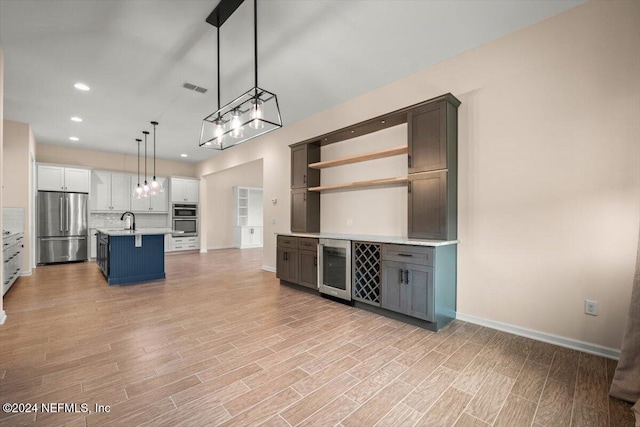 kitchen featuring sink, hanging light fixtures, appliances with stainless steel finishes, white cabinetry, and beverage cooler