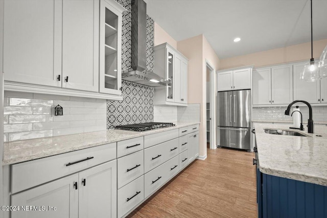 kitchen with stainless steel appliances, sink, wall chimney range hood, pendant lighting, and white cabinets