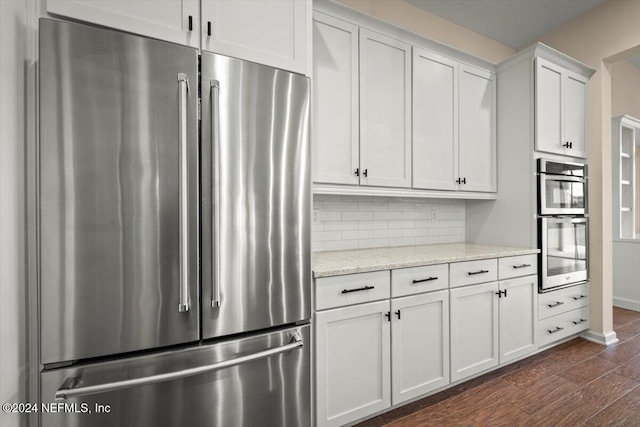 kitchen with light stone countertops, appliances with stainless steel finishes, tasteful backsplash, dark hardwood / wood-style flooring, and white cabinetry