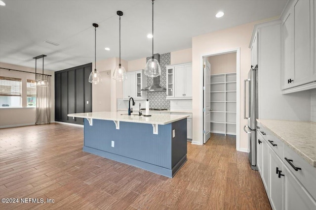 kitchen featuring a kitchen breakfast bar, pendant lighting, decorative backsplash, a center island with sink, and white cabinets