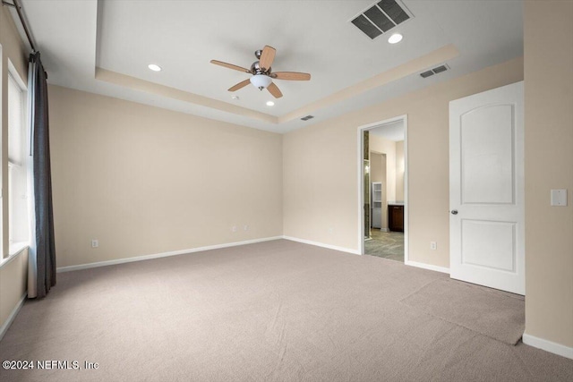 carpeted spare room featuring a tray ceiling and ceiling fan