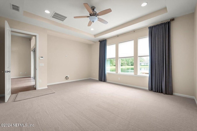 spare room featuring ceiling fan, light carpet, and a tray ceiling