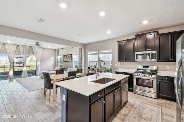 kitchen featuring sink, ceiling fan, stainless steel appliances, dark brown cabinetry, and an island with sink