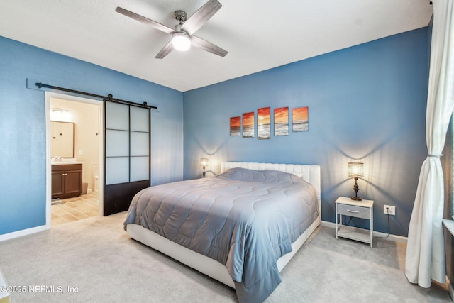 bedroom with ceiling fan, a barn door, light colored carpet, and ensuite bath