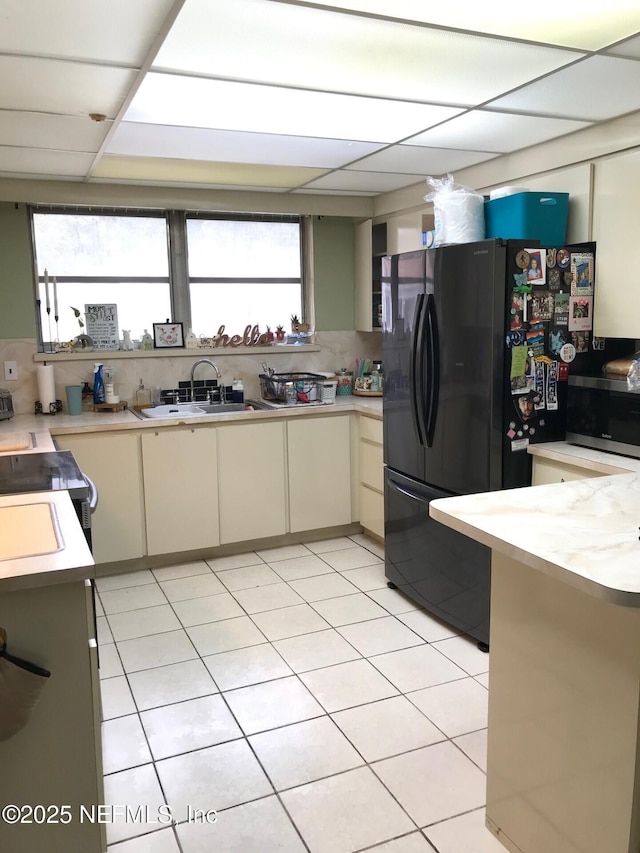 kitchen featuring backsplash, black refrigerator, sink, and cream cabinets