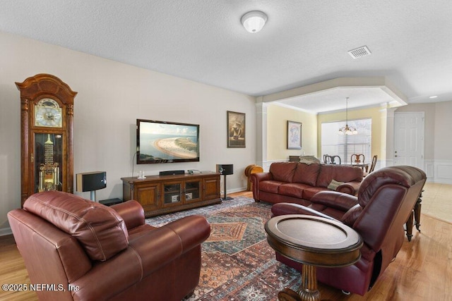 living room featuring hardwood / wood-style floors, a textured ceiling, a chandelier, and ornate columns