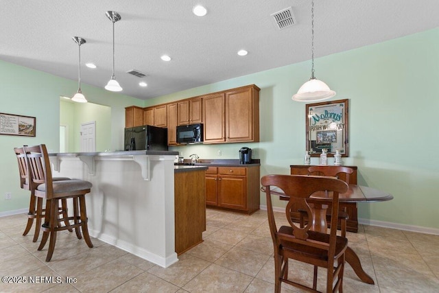 kitchen with a textured ceiling, black appliances, a center island, a kitchen bar, and hanging light fixtures