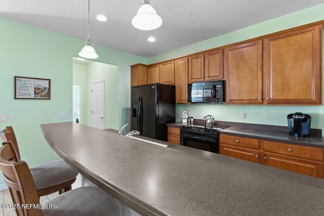 kitchen with a breakfast bar area, hanging light fixtures, a textured ceiling, black appliances, and sink