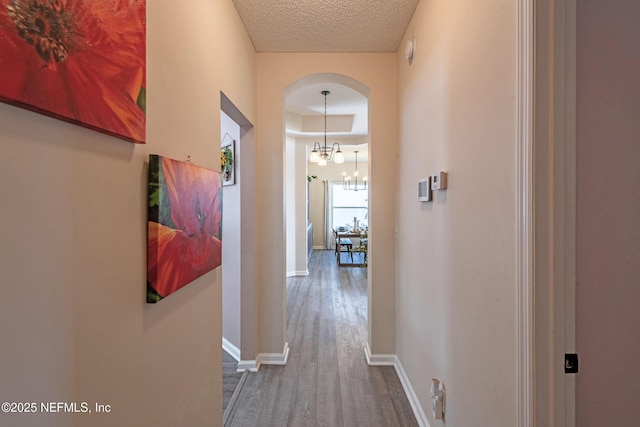 hallway featuring an inviting chandelier, a textured ceiling, and hardwood / wood-style flooring