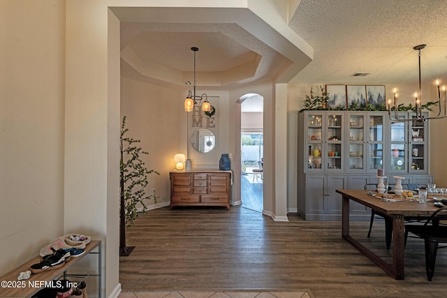 dining room featuring a chandelier, dark hardwood / wood-style flooring, a textured ceiling, and a raised ceiling