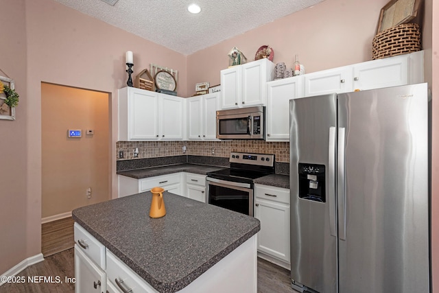 kitchen with appliances with stainless steel finishes, dark hardwood / wood-style flooring, a textured ceiling, a center island, and white cabinetry