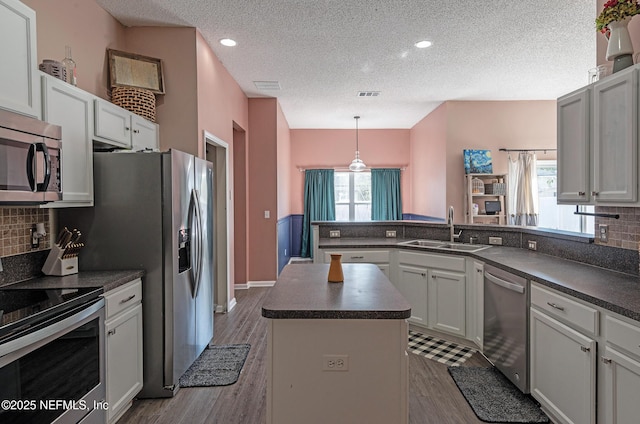 kitchen featuring sink, a center island, dark wood-type flooring, a textured ceiling, and appliances with stainless steel finishes