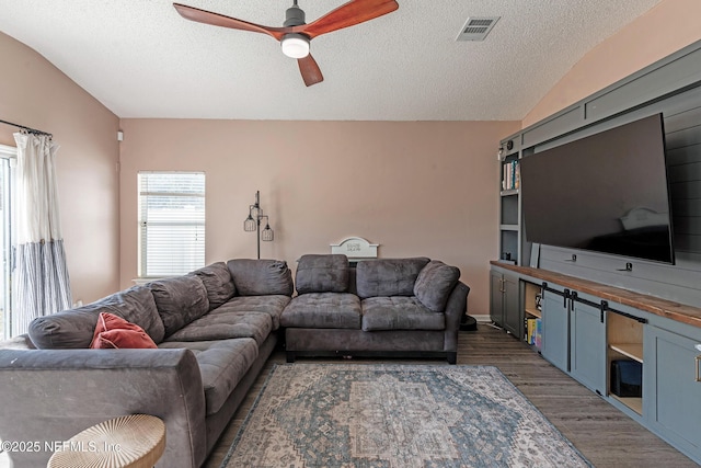 living room with a textured ceiling, dark hardwood / wood-style floors, vaulted ceiling, and ceiling fan