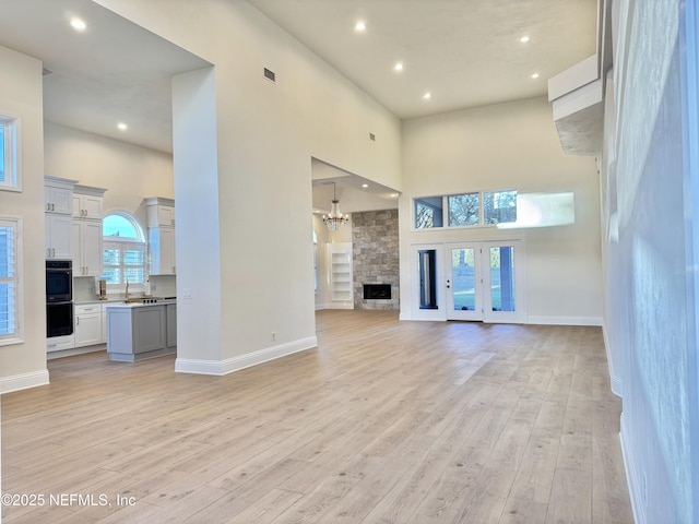 unfurnished living room with a high ceiling, light wood-type flooring, a stone fireplace, and a wealth of natural light