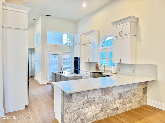 kitchen with sink, kitchen peninsula, white cabinets, light hardwood / wood-style floors, and a high ceiling