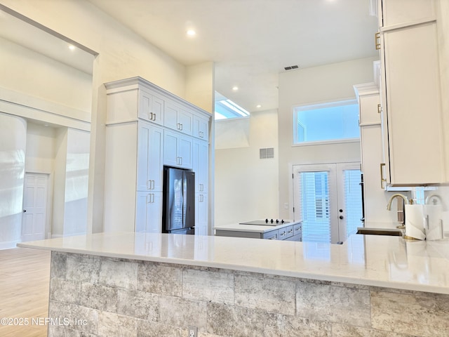 kitchen with sink, light stone counters, black electric cooktop, stainless steel fridge, and kitchen peninsula