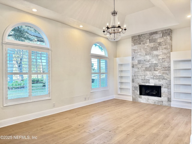 unfurnished living room featuring an inviting chandelier, a large fireplace, a raised ceiling, built in features, and light hardwood / wood-style floors