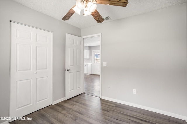 unfurnished bedroom featuring a textured ceiling, dark wood-style floors, visible vents, and baseboards