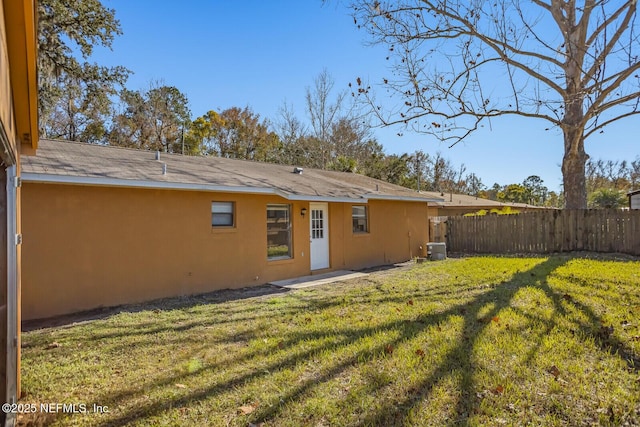 back of property featuring fence, stucco siding, a lawn, and central AC unit