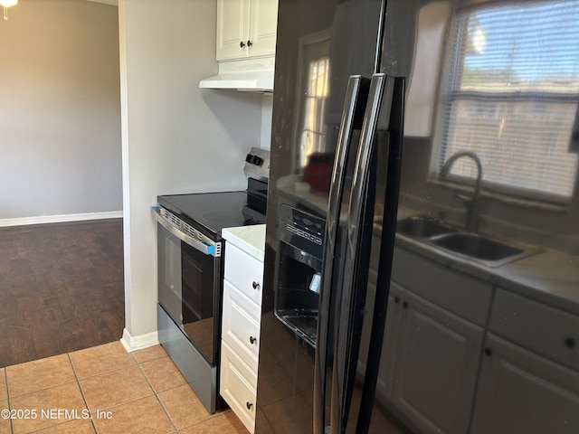 kitchen featuring under cabinet range hood, stainless steel range with electric stovetop, white cabinets, and a sink