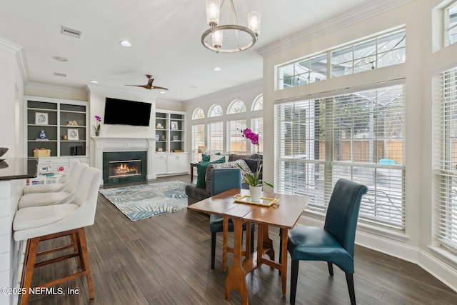 dining area with a wealth of natural light, dark hardwood / wood-style flooring, crown molding, and ceiling fan with notable chandelier