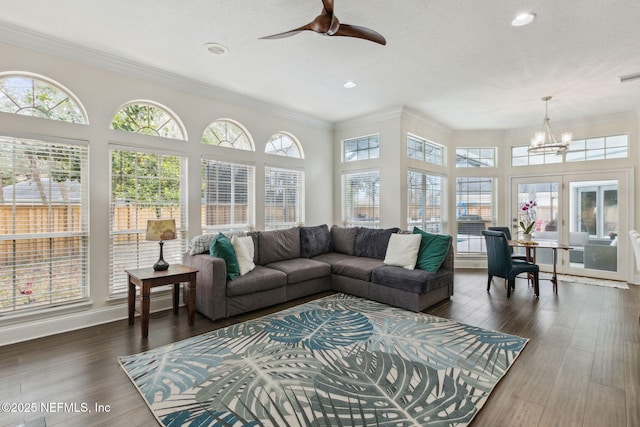 living room with crown molding, dark wood-type flooring, a healthy amount of sunlight, and ceiling fan with notable chandelier