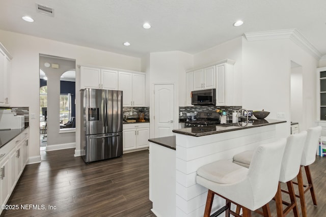 kitchen featuring white cabinetry, dark wood-type flooring, kitchen peninsula, a breakfast bar area, and appliances with stainless steel finishes