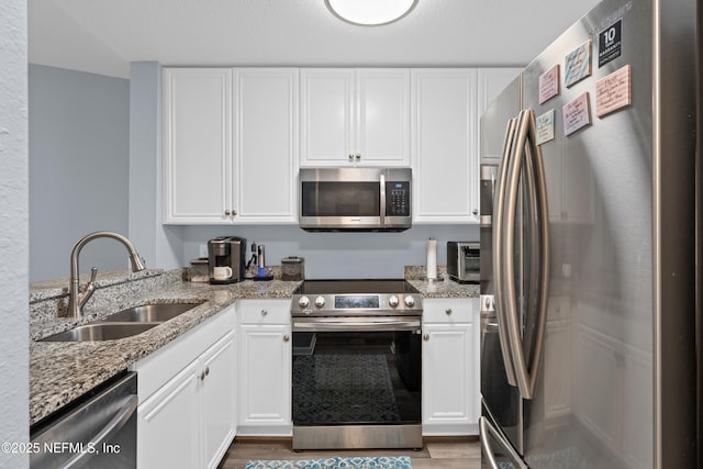 kitchen featuring light stone counters, light hardwood / wood-style flooring, stainless steel appliances, white cabinetry, and sink