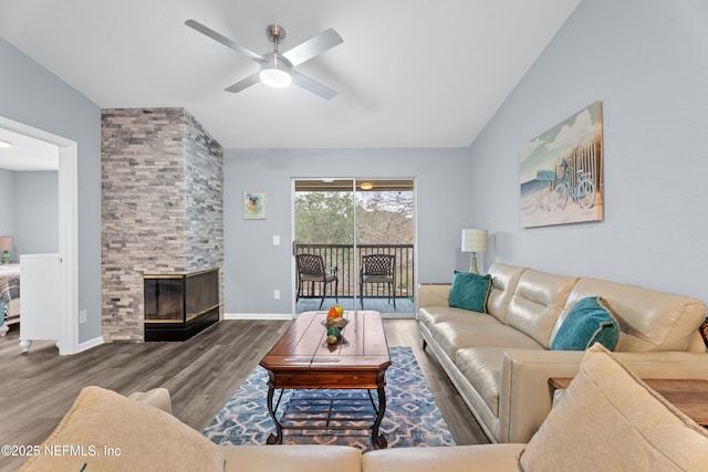 living room with lofted ceiling, wood-type flooring, ceiling fan, and a stone fireplace