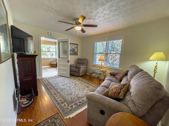 living room featuring ceiling fan, wood-type flooring, plenty of natural light, and a textured ceiling