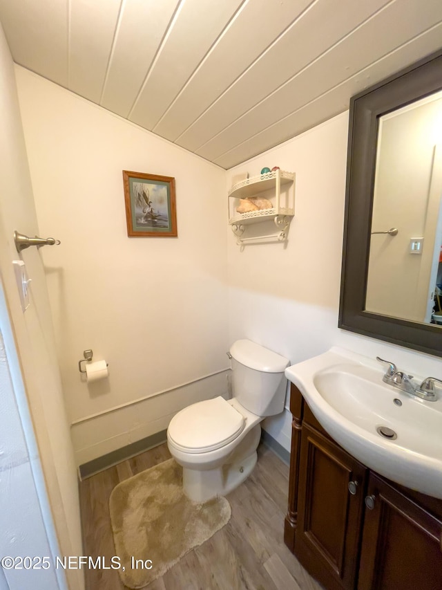 bathroom featuring hardwood / wood-style flooring, vanity, toilet, and lofted ceiling