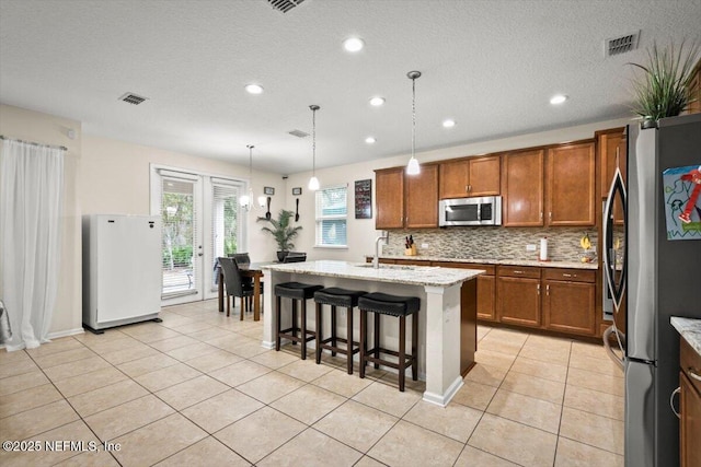 kitchen featuring sink, hanging light fixtures, an island with sink, a kitchen bar, and stainless steel appliances