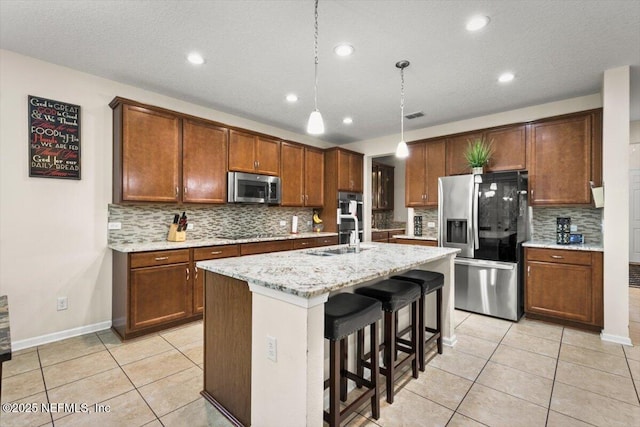 kitchen featuring hanging light fixtures, light tile patterned floors, an island with sink, a kitchen bar, and stainless steel appliances