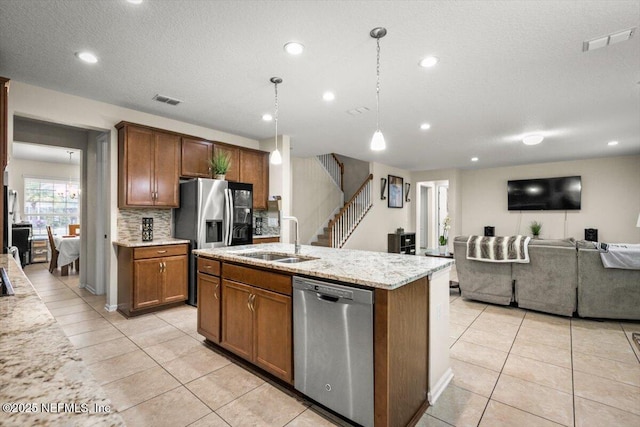 kitchen featuring light stone countertops, appliances with stainless steel finishes, sink, decorative light fixtures, and an island with sink