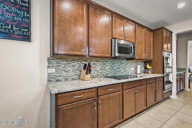 kitchen featuring stainless steel appliances, tasteful backsplash, light stone counters, a textured ceiling, and light tile patterned flooring